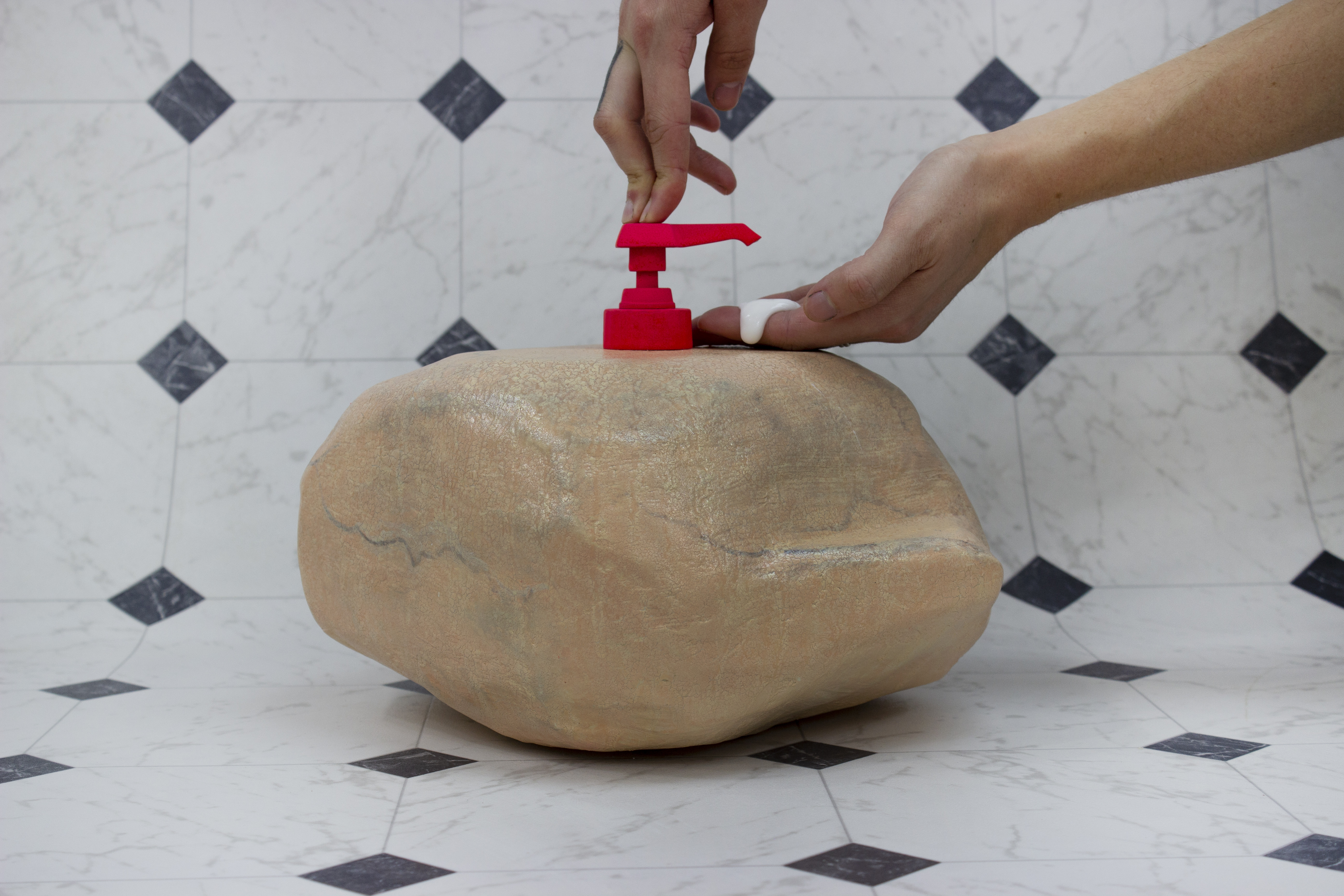 a rock with a lotion dispenser in it, applying lotion to a hand